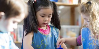 Young children wearing aprons are playing with a water table together in nursery.